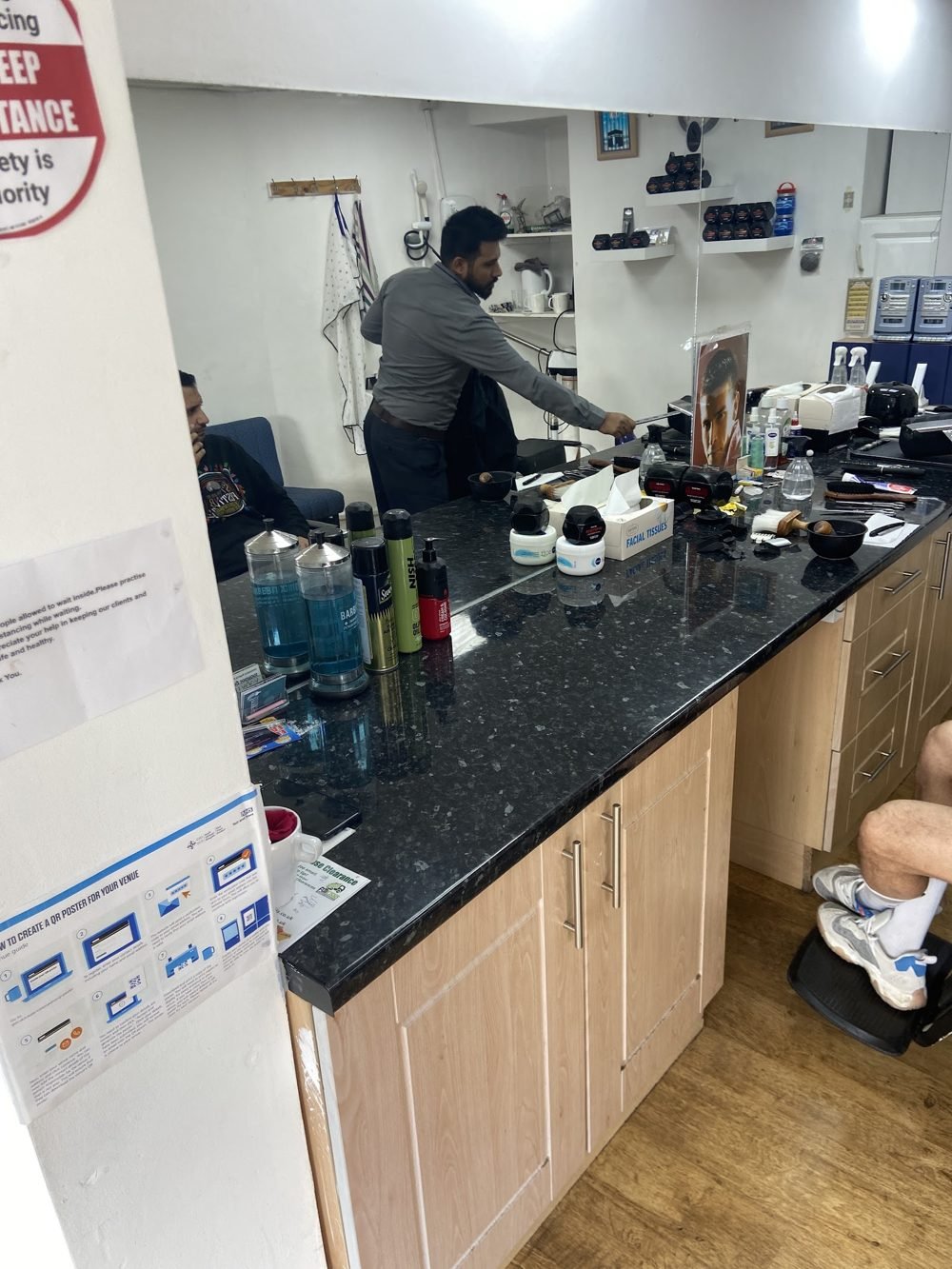 A barber working at the counter inside the shop, clippers and products laid out