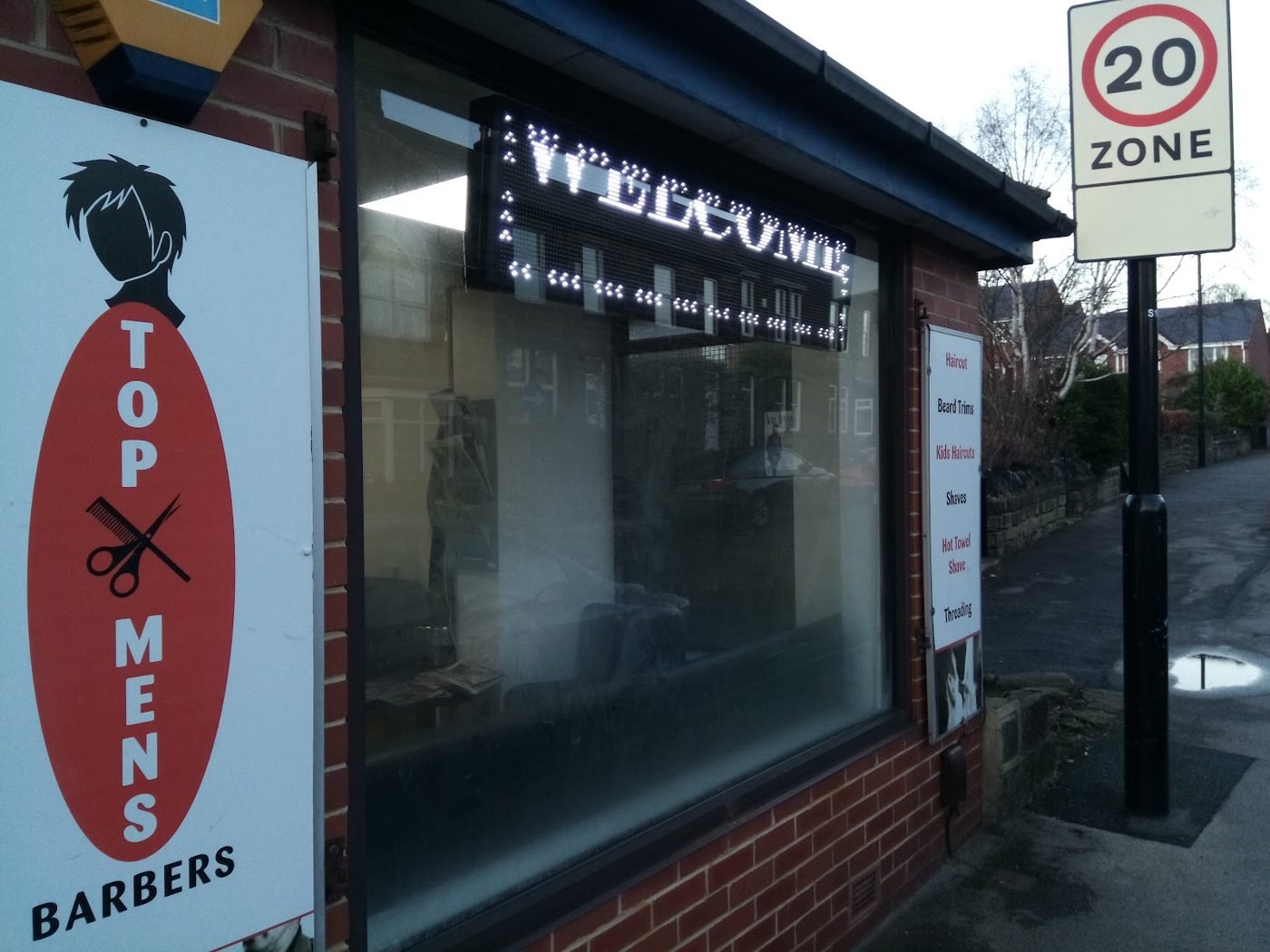 The shopfront on Sunnybank Avenue: red oval Top Men's Barbers sign beside a window with a WELCOME light